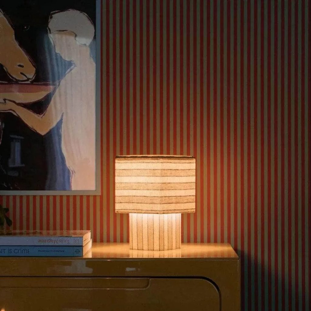 Table lamp with warm light on a sideboard, with striped wallpaper as a backdrop
